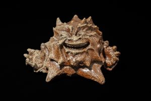 A strange ceramic character that looks a bit like a star with lots of spikes and a laughing face on a black background