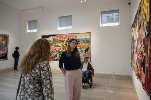 Four people looking on at three tapestries around a large white gallery