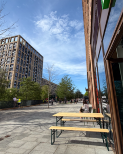 On the left a big block of flats, on the right the front of a cafe, separated by an open pedestrianised area on a sunny day.