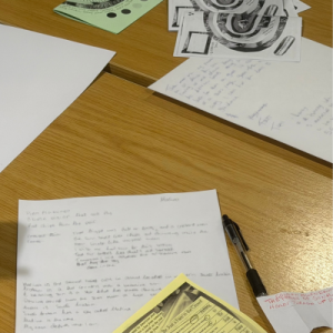 Looking down on a pale wooden table with pieces of paper, a pen and writing apparel