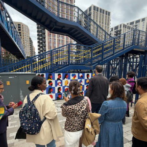 A group of people from behind looking on to a blue bridge with an artwork comprising of lots of portraits