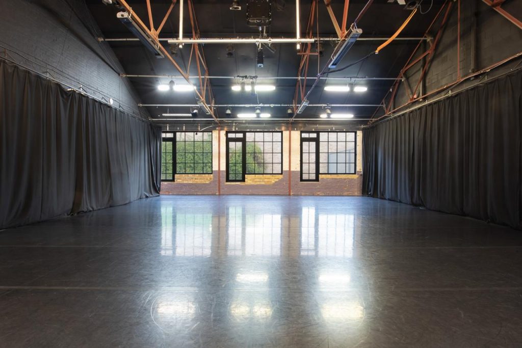 A large room with long grey curtains on either side and black window frames looking onto a green and brown outside space in the background.