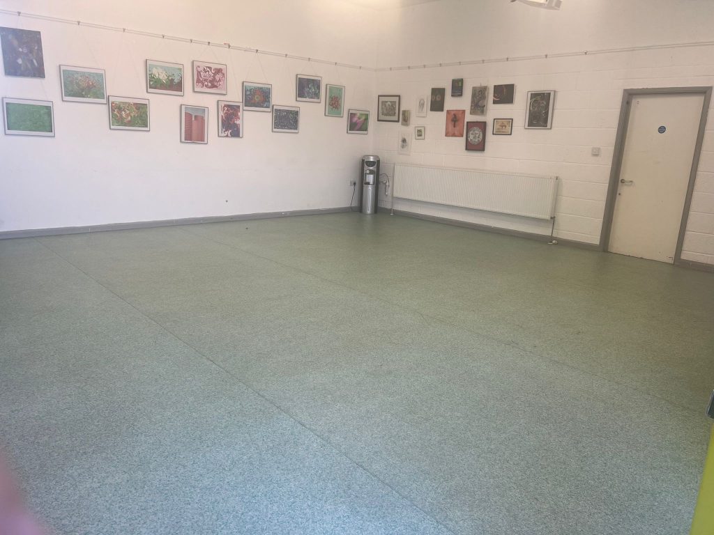 A large empty room with light green tiled flooring, white walls and lots of framed artworks on the wall