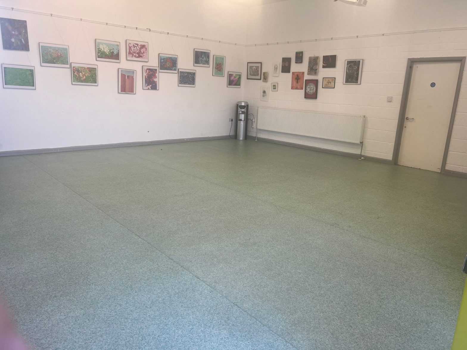 A large empty room with light green tiled flooring, white walls and lots of framed artworks on the wall