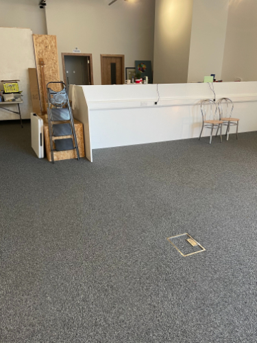 An empty studio space with grey floors, white walls and a few items including chairs and wooden planks laying around