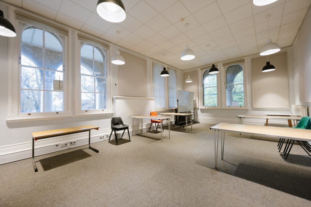 Well lit meeting room with tables, a few chairs, and windows