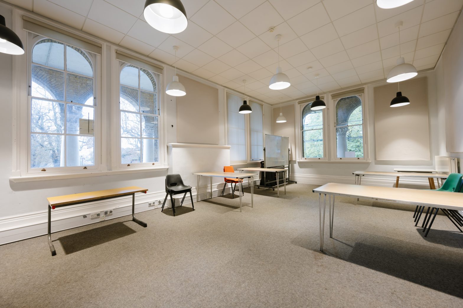 Well lit meeting room with tables, a few chairs, and windows
