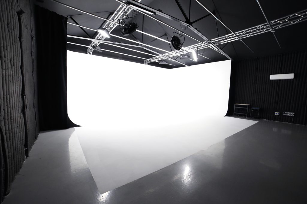 A large white infinity wall and flooring in an otherwise black studio with metal rigging on the ceiling