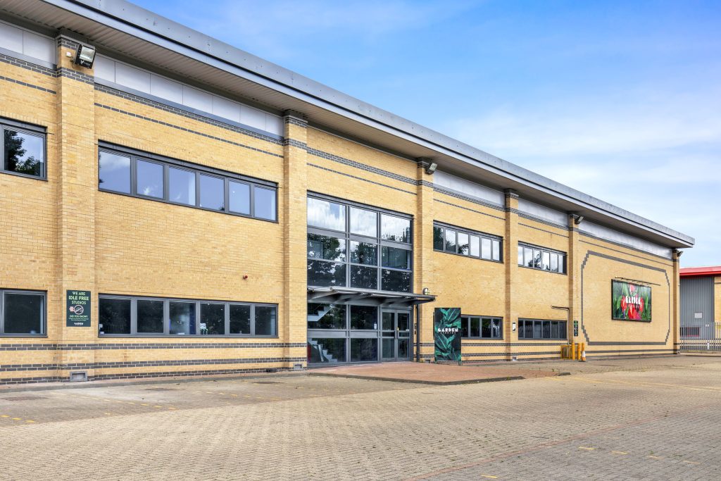 The exterior of a pale bricked modern building with two rows of windows and a glassed entrance in the middle on a sunny day
