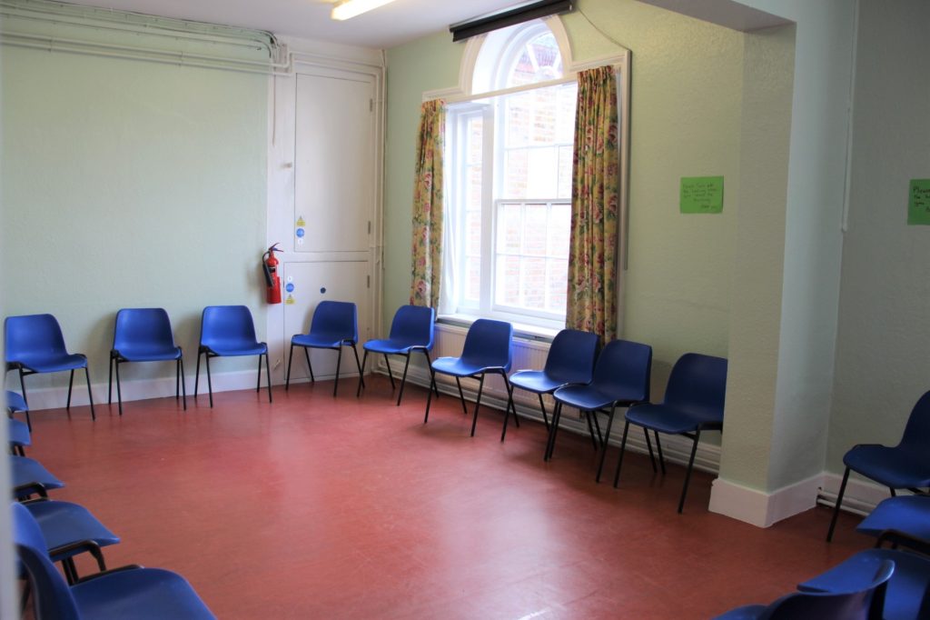Lots of blue chairs around the perimeter of a room with a red floor, light green walls and a window