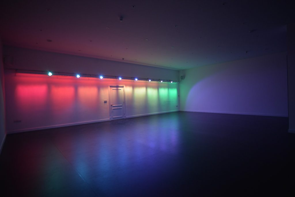 Gree, yellow and red lights light up an empty studio space with dark flooring