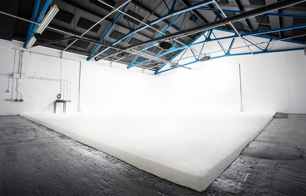 A studio with white floor and walls, a dark ceiling with blue rigging on