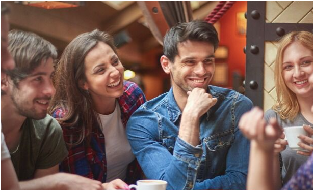 Five young adults laughing and smiling wearing casual clothing two are holding coffee cups