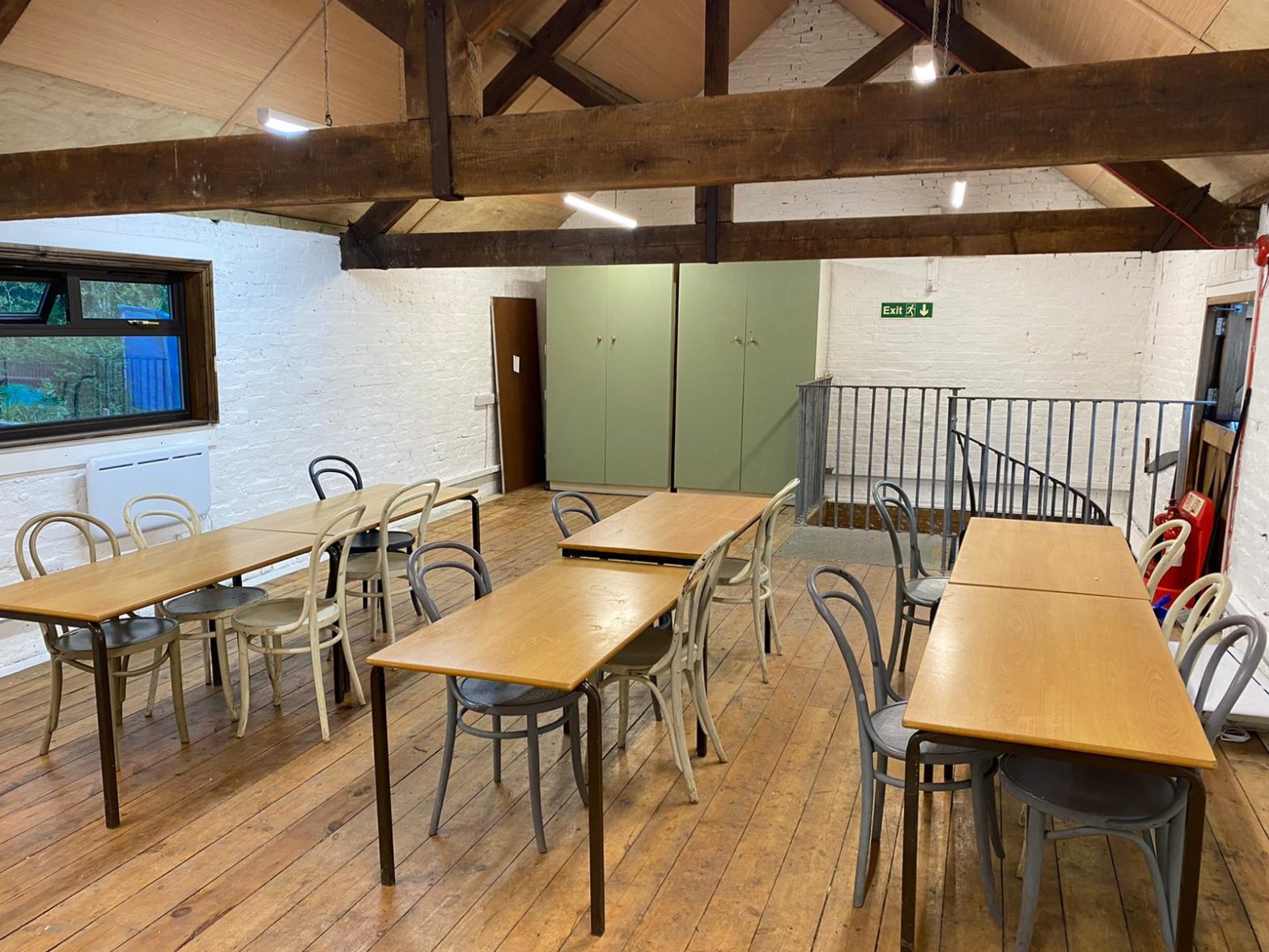 Indoor space, wooden floors, tables and chairs arranged in rows, classroom style. Rafters overhead.