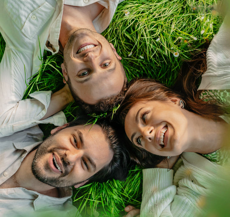 Three people lying down, photo taken from above, their heads are together and they are lying on grass