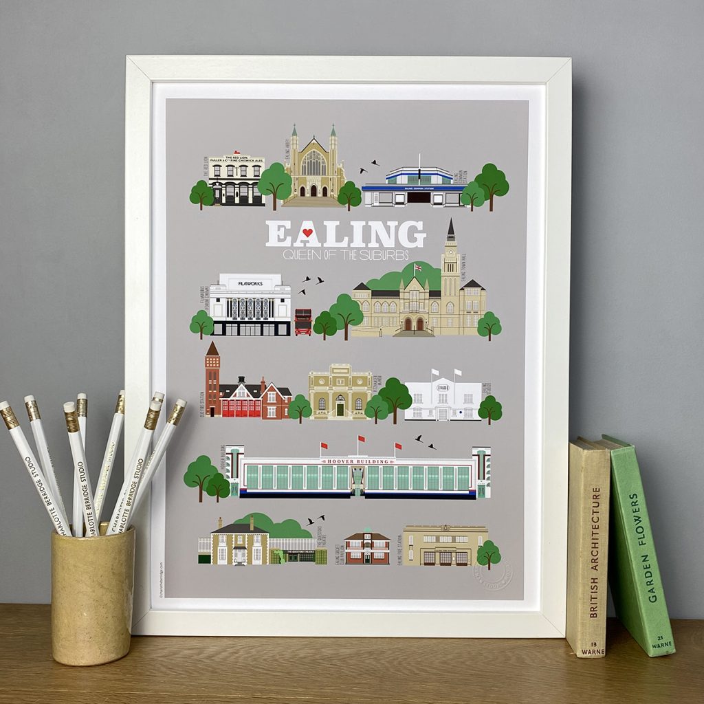 A white frame holds a picture of places in Ealing, it's on a wooden shelf with pencils and two books to the side