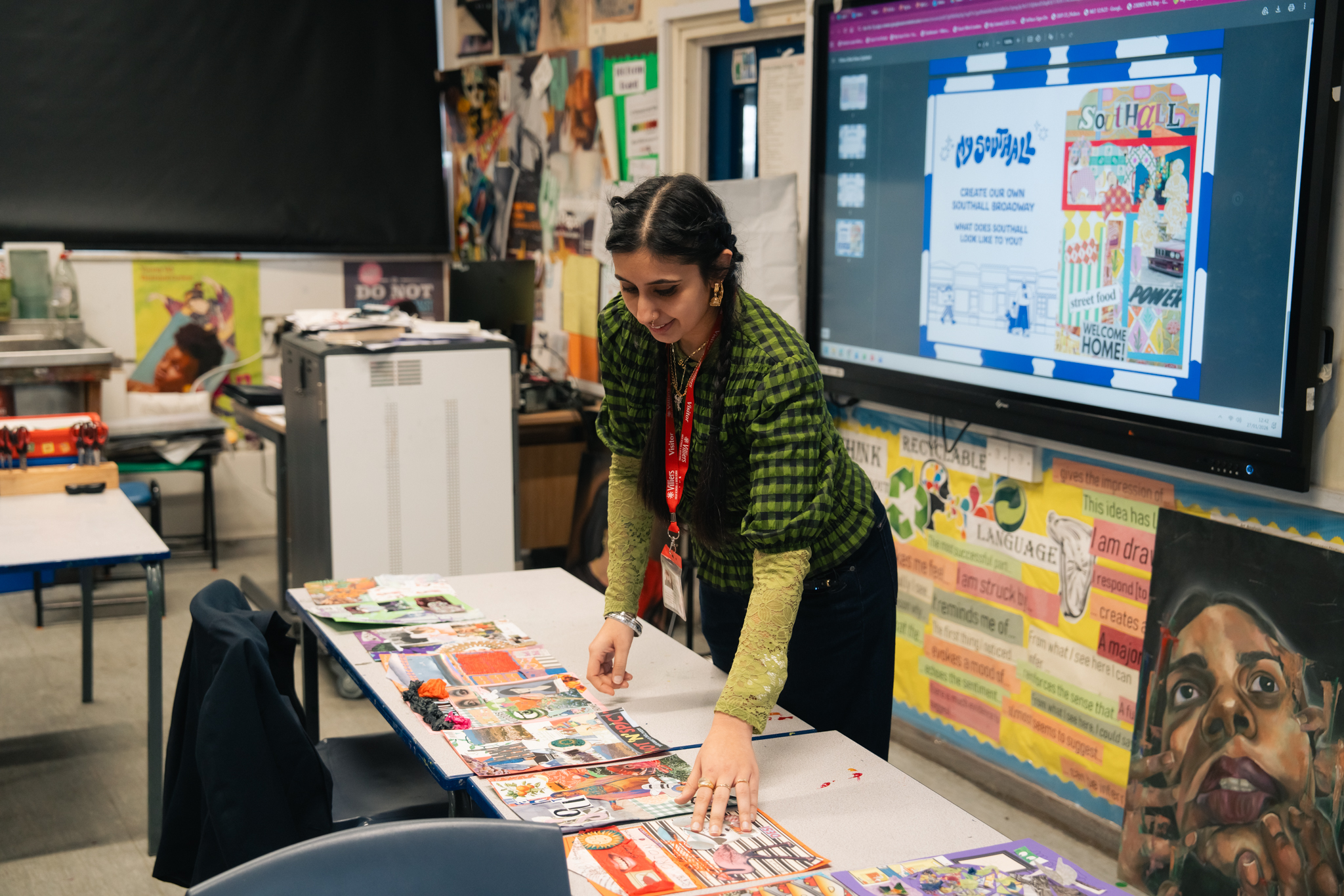 A woman leans over a table with craft materials on in a school classroom