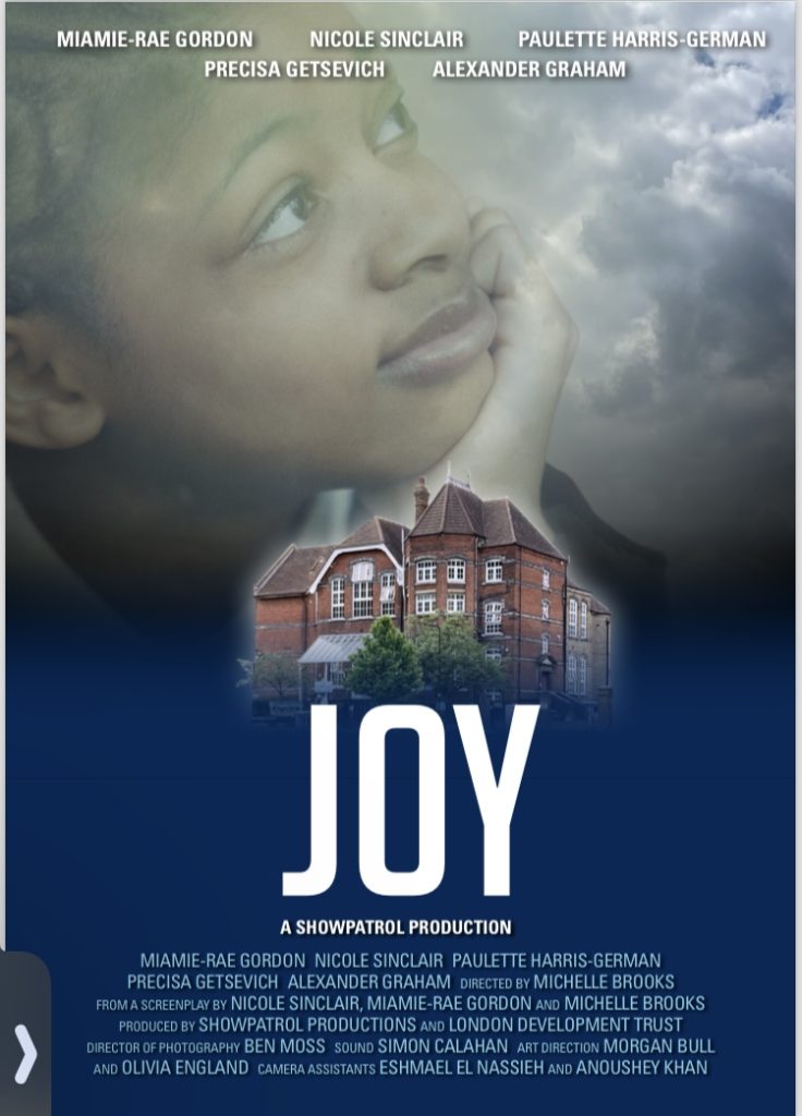 A film poster for a film called 'Joy' with white writing on a blue background at the bottom and a girls face in her hand, smiling and looking up at a stormy sky and an image of a large modern house in the middle