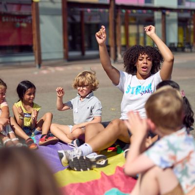 a group of small children sat down in a circle on a blanket outside playing