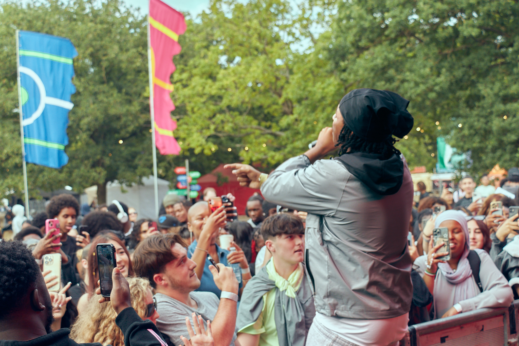 A young woman with long black hair has her back to us as she performs on stage to a full audience at a festival in a field - New Gen Festival