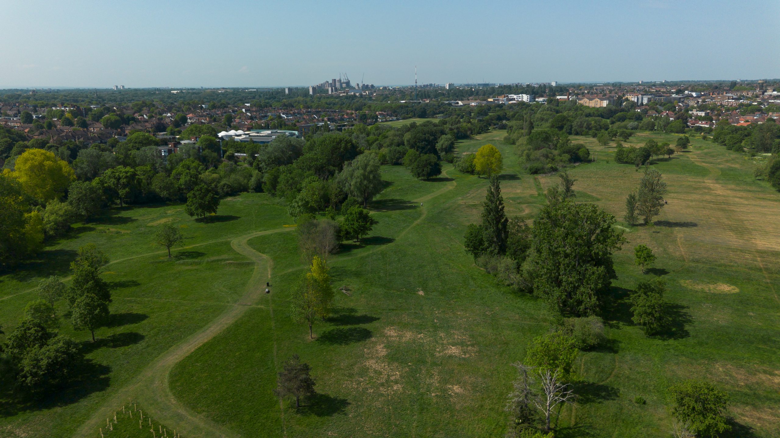 An aerial shot of a large green park with grassy fields and green trees under a blue sky