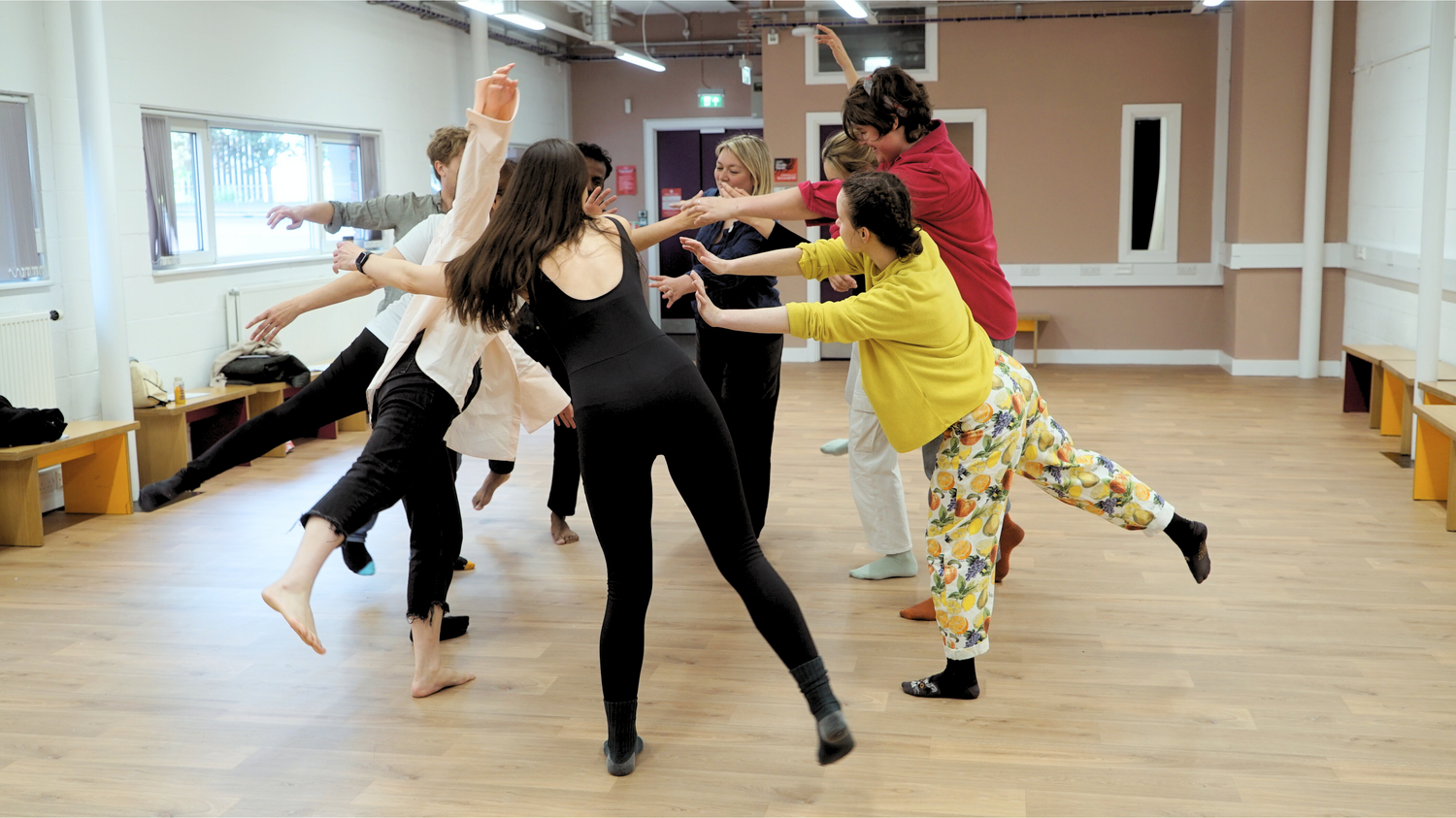 9 people in a circle balancing on one foot in a studio